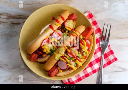 Chiens chipants de fantaisie recouverts de radis, de ketchup à la moutarde et de vert sauce sur des petits pains sans gluten Banque D'Images