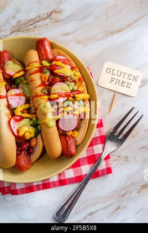 Chiens chipants de fantaisie recouverts de radis, de ketchup à la moutarde et de vert sauce sur des petits pains sans gluten Banque D'Images