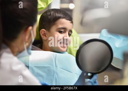 Un garçon, enfant avec un dentiste, regarde ses dents dans le miroir Banque D'Images