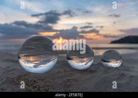 Trois boules de cristal claires de trois tailles sont sphérique révèle vue paysage avec sphérique placé sur le sable à Karon Beach pendant le coucher du soleil. Banque D'Images