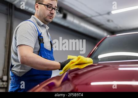 L'homme après le lavage essuie la voiture rouge avec un chiffon au lavage de voiture. Main mâle et carrosserie de voiture de près Banque D'Images