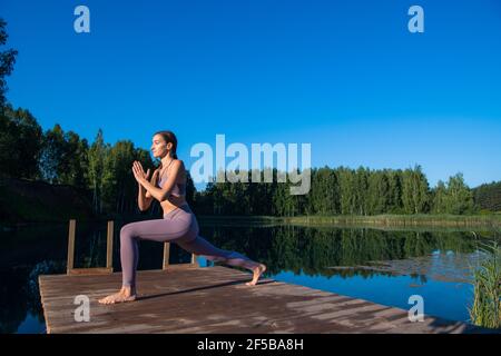 Jeune femme pratiquant le yoga contre le ciel au lever du soleil. Une femme plutôt fine fait un exercice. Concept de santé, méditation, bien-être, pleine conscience Banque D'Images