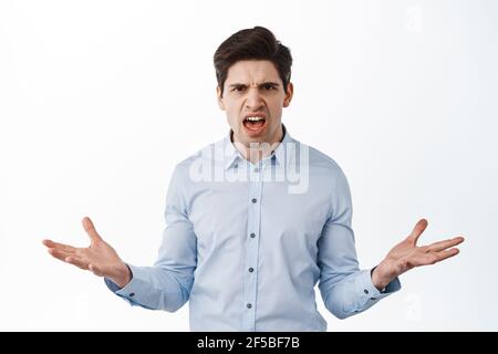 Homme d'affaires en colère et frustré, employé de bureau se plaignant, semblent confus et mécontent, arguant, se tenant contre fond blanc Banque D'Images