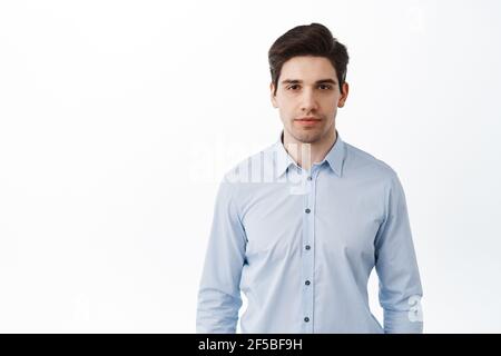 Portrait d'un employé de bureau, homme d'affaires entrepreneur debout dans un col bleu chemise avec un visage sérieux, des cercles sombres sous les yeux, aspect fatigué, blanc Banque D'Images