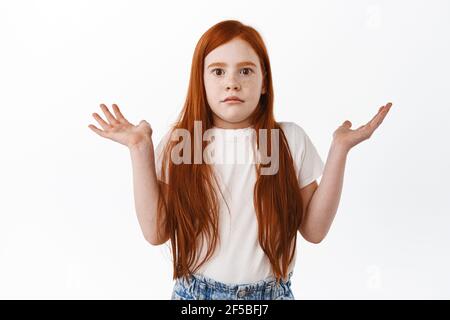 Enfant ne sait pas. Mignon redhead petite fille haussant les mains vers le haut, regarde sans indice et confus à l'appareil-photo, n'ont aucune idée, ne peut pas comprendre quelque chose Banque D'Images