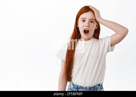 N'oubliez pas. Mignon redhead petite fille, enfant avec de longs cheveux de gingembre et les taches de rousseur oubliées, tenant la main sur la tête et dire aïe, bpoint dans quelque chose Banque D'Images