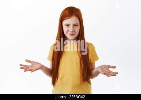 Belle petite fille caucasienne avec des taches de rousseur, des cheveux de gingembre, haussiers, écartez les mains et regardez confus, demandant ce que, ne sais pas comprendre, debout Banque D'Images