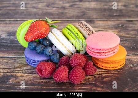 Délicieux macarons et baies sauvages, bleuets et framboises sur fond de bois. Banque D'Images