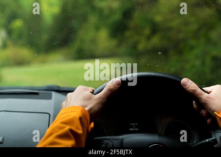 Gros plan des mains du conducteur sur le volant de direction conduite d'une voiture moderne tout-terrain conduite à droite sur la route de campagne verte de montagne. Insid Banque D'Images