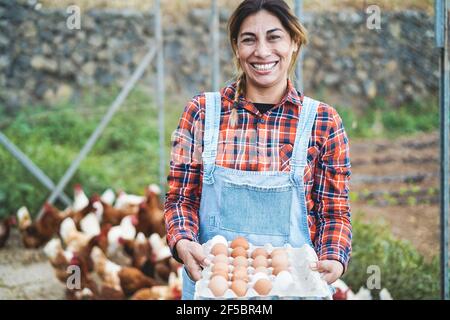 Femme agricole senior qui prend des œufs biologiques dans le poulailler - Mode de vie agricole et concept d'alimentation saine - accent sur le visage Banque D'Images