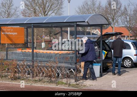 Un couple âgé au supermarché a chargé des provisions dans sa voiture, m, la femme retourne le chariot vide à un abri couvert pour chariots Banque D'Images