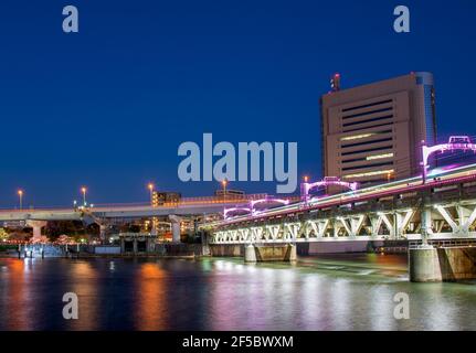 Train de vitesse traversant un pont illuminé enjambant une rivière puissante sous un ciel dégagé la nuit Banque D'Images