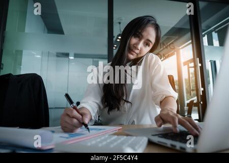 Femme d'affaires tenant le stylo et pointant vers la paperasse financière avec le schéma de réseau financier. Banque D'Images