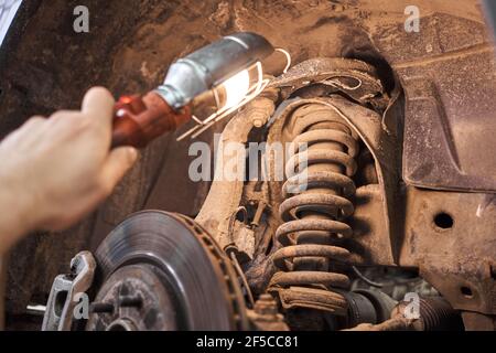 Un mécanicien inspecte l'amortisseur, les ressorts et les barres stabilisatrices à l'aide d'une lampe de poche. Voiture sur un banc de réparation. Station de service technique pour voiture. Banque D'Images