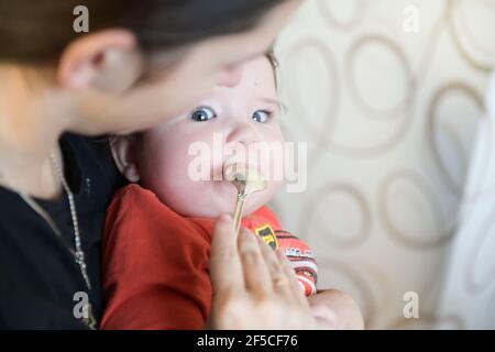 maman nourrit le bébé avec une cuillère sur ses genoux. Maman nourrit le porridge de son petit fils avec une cuillère. Un petit déjeuner équilibré de porridge pour le jeune organisme Banque D'Images