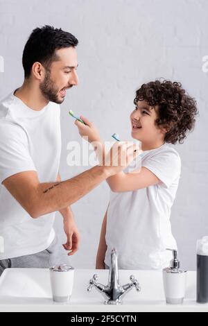 Père et garçon arabes tenant des brosses à dents près de l'évier et du robinet Banque D'Images