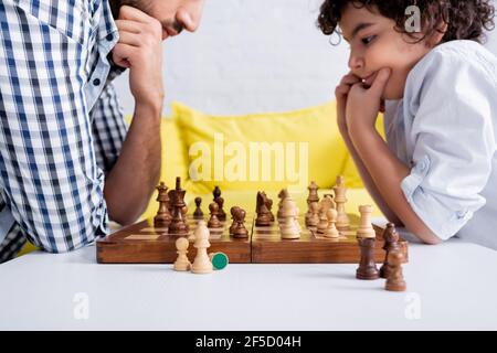 Échecs à bord près d'un garçon arabe pensif jouant avec son père sur un arrière-plan flou Banque D'Images