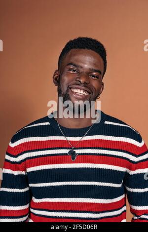 Photo de l'homme noir smiley posant en studio et regardant l'appareil photo sur fond marron. Banque D'Images