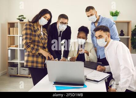 Groupe d'étudiants ou équipe d'affaires dans le masque facial regardant le webinaire sur ordinateur portable au bureau Banque D'Images