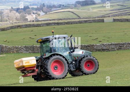 Agriculteur qui conduit un tracteur Hurlimann, étalant de l'engrais sur une prairie en montagne au printemps, dans le North Yorkshire, au Royaume-Uni. Banque D'Images