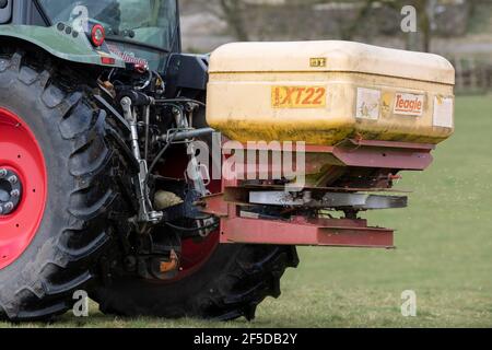 Agriculteur qui conduit un tracteur Hurlimann, étalant de l'engrais sur une prairie en montagne au printemps, dans le North Yorkshire, au Royaume-Uni. Banque D'Images