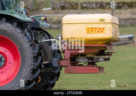 Agriculteur qui conduit un tracteur Hurlimann, étalant de l'engrais sur une prairie en montagne au printemps, dans le North Yorkshire, au Royaume-Uni. Banque D'Images