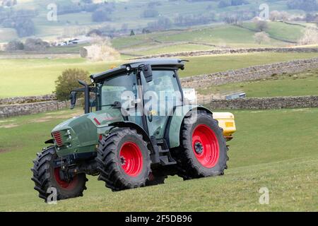 Agriculteur qui conduit un tracteur Hurlimann, étalant de l'engrais sur une prairie en montagne au printemps, dans le North Yorkshire, au Royaume-Uni. Banque D'Images