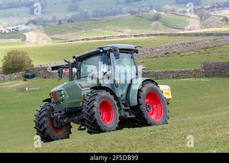 Agriculteur qui conduit un tracteur Hurlimann, étalant de l'engrais sur une prairie en montagne au printemps, dans le North Yorkshire, au Royaume-Uni. Banque D'Images