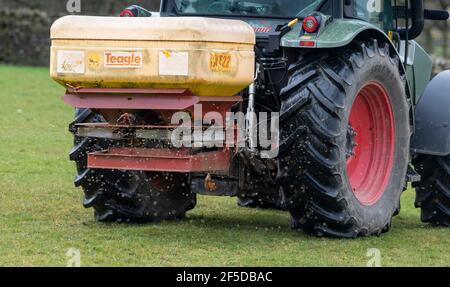 Agriculteur qui conduit un tracteur Hurlimann, étalant de l'engrais sur une prairie en montagne au printemps, dans le North Yorkshire, au Royaume-Uni. Banque D'Images