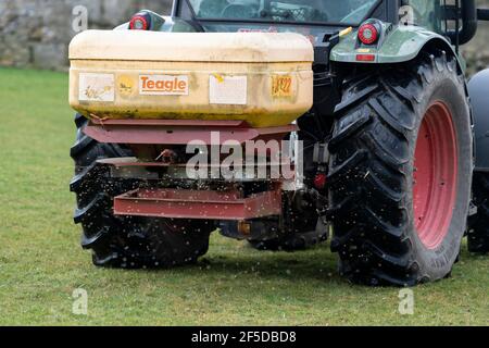 Agriculteur qui conduit un tracteur Hurlimann, étalant de l'engrais sur une prairie en montagne au printemps, dans le North Yorkshire, au Royaume-Uni. Banque D'Images