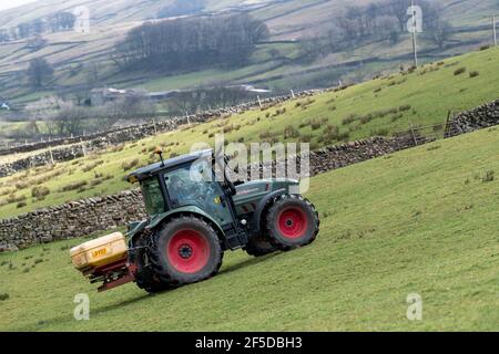 Agriculteur qui conduit un tracteur Hurlimann, étalant de l'engrais sur une prairie en montagne au printemps, dans le North Yorkshire, au Royaume-Uni. Banque D'Images