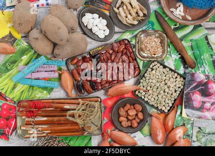 Étalage de semis de printemps : paquets de semences, pommes de terre de semence, ensemble d'échalotes, étiquettes de plantes, dibber, et de la courgette, de la panais, du radis, du pois, du coureur et des graines de haricots Banque D'Images