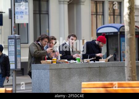 Des hommes travaillant dans Cannon Street, dans le quartier financier de la ville de Londres, buvant du café et déjeunent en plein air, au mur, tout en regardant l'écran du téléphone Banque D'Images