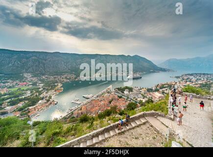 Un bateau de croisière attend, ancré sur la baie, vu de la forteresse de Kotor, et les touristes marchent les ruines de la bataille sur le point de vue de la colline à l'approche du coucher du soleil Banque D'Images