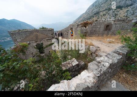 Les touristes visitent les ruines historiques et anciennes de la forteresse de Kotor qui se dresse au sommet d'une colline surplombant la baie en contrebas. Banque D'Images