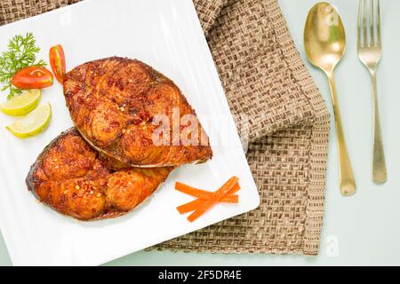 Faites frire le poisson sur une assiette en céramique carrée blanche et ajoutez-y des tranches d'oignon, de citron et de tomate. Banque D'Images