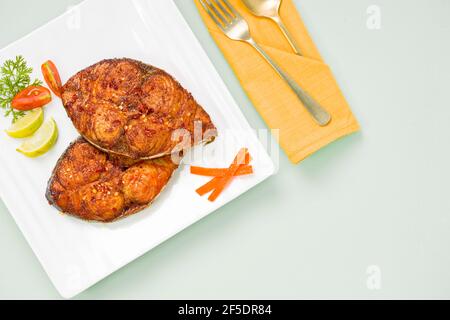 Faites frire le poisson sur une assiette en céramique carrée blanche et ajoutez-y des tranches d'oignon, de citron et de tomate. Banque D'Images