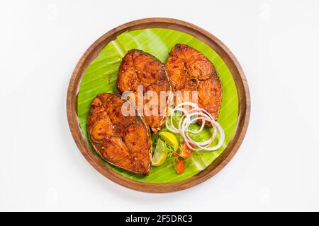 Poêler le poisson joliment arrangé et garni de tranches d'oignon, de citron et de tomate sur une assiette en bois bordée de feuilles de banane. Banque D'Images