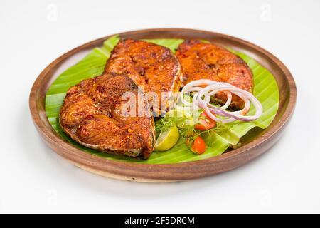 Poêler le poisson joliment arrangé et garni de tranches d'oignon, de citron et de tomate sur une assiette en bois bordée de feuilles de banane. Banque D'Images