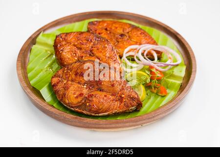 Poêler le poisson joliment arrangé et garni de tranches d'oignon, de citron et de tomate sur une assiette en bois bordée de feuilles de banane. Banque D'Images