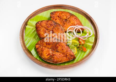 Poêler le poisson joliment arrangé et garni de tranches d'oignon, de citron et de tomate sur une assiette en bois bordée de feuilles de banane. Banque D'Images