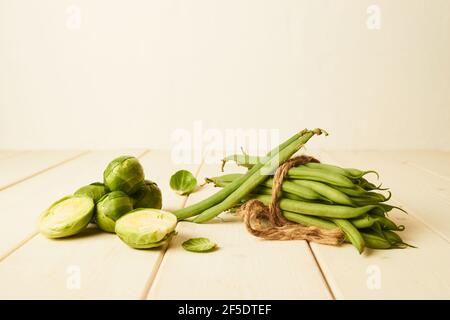 Haricots verts crus liés à une corde AT et à des pousses de Brussel placé sur une table en bois Banque D'Images