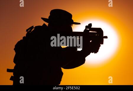 Silhouette du commando des forces spéciales de l'armée, soldat en chapeau de boonie visant et tirant sur le canon de sous-machine bullpup sur fond de soleil couchant. Compagnie militaire privée mercenaire engageant l'ennemi au coucher du soleil Banque D'Images