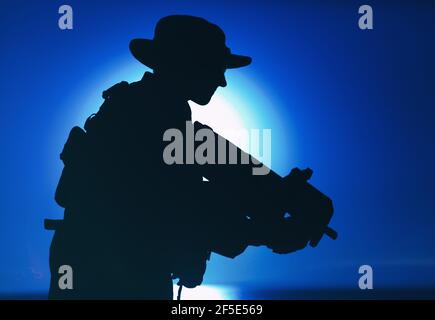 Silhouette du commando des forces spéciales de l'armée, soldat en chapeau de boonie visant et tirant sur le canon de sous-machine bullpup sur fond de soleil couchant. Compagnie militaire privée mercenaire engageant l'ennemi au coucher du soleil Banque D'Images