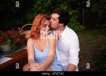 Un jeune homme brunette embrasse doucement une belle fille aux cheveux rouges sur le front, elle rit. Portrait rapproché de couple amoureux, reposant sur un pique-nique à Banque D'Images