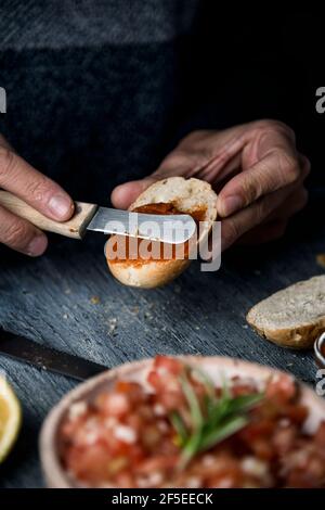 un jeune caucasien répand une version végétalienne de la sobrasada espagnole, faite avec des tomates séchées et des amandes, sur un pain grillé coupé en deux, sur un gr Banque D'Images