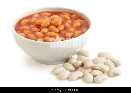 Haricots cuits à la sauce tomate dans un bol en céramique blanc à côté de haricots haricates non cuits isolés sur du blanc. Banque D'Images
