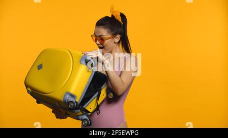 femme excitée tenant une valise isolée sur jaune Banque D'Images