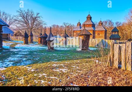 Regardez les ruches traditionnelles dans l'ancienne ferme de la région de Polissya avec l'église de la Résurrection en bois, vue derrière la clôture, Pyrohiv Skansen, Kiev, Royaume-Uni Banque D'Images