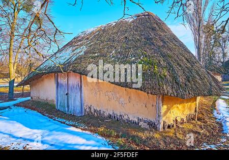 Le bâtiment historique de la grange d'argile avec un toit de paille au milieu de la cour enneigée sur le terrain de Pyrohiv Skansen, Kiev, Ukraine Banque D'Images